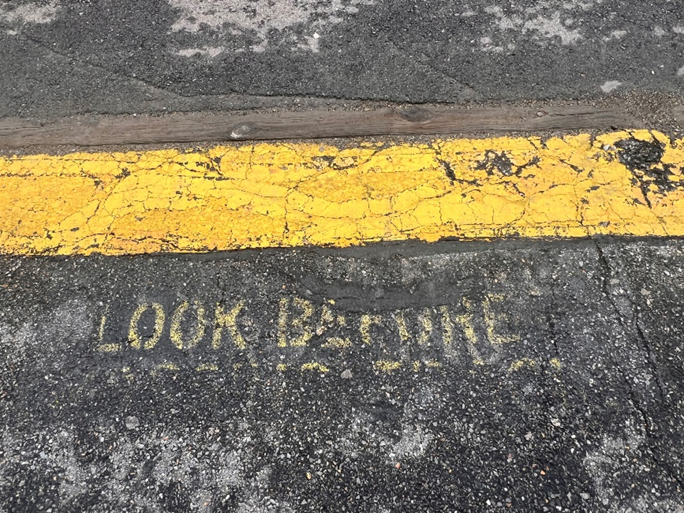 This image shows worn, faded pavement markings at a train crossing at Ayer station.