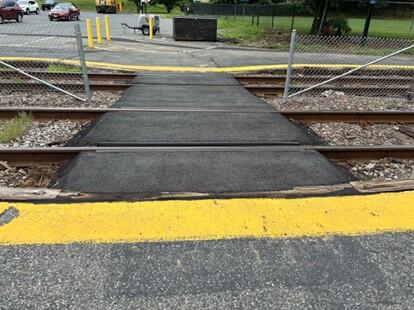 This image shows worn, faded pavement markings at a train crossing at Brandeis/Roberts station.