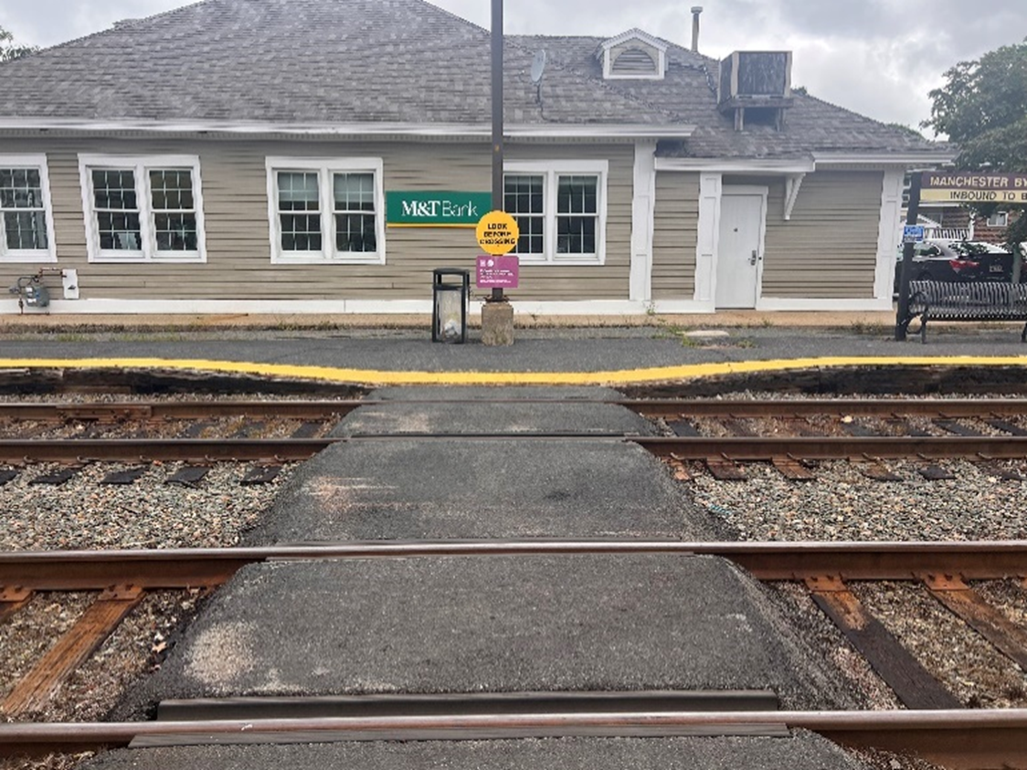 This image shows a “Look Before Crossing” sign at the far side of a train crossing at Manchester station. This image shows the far side of a train crossing with no crossing sign at Manchester station.