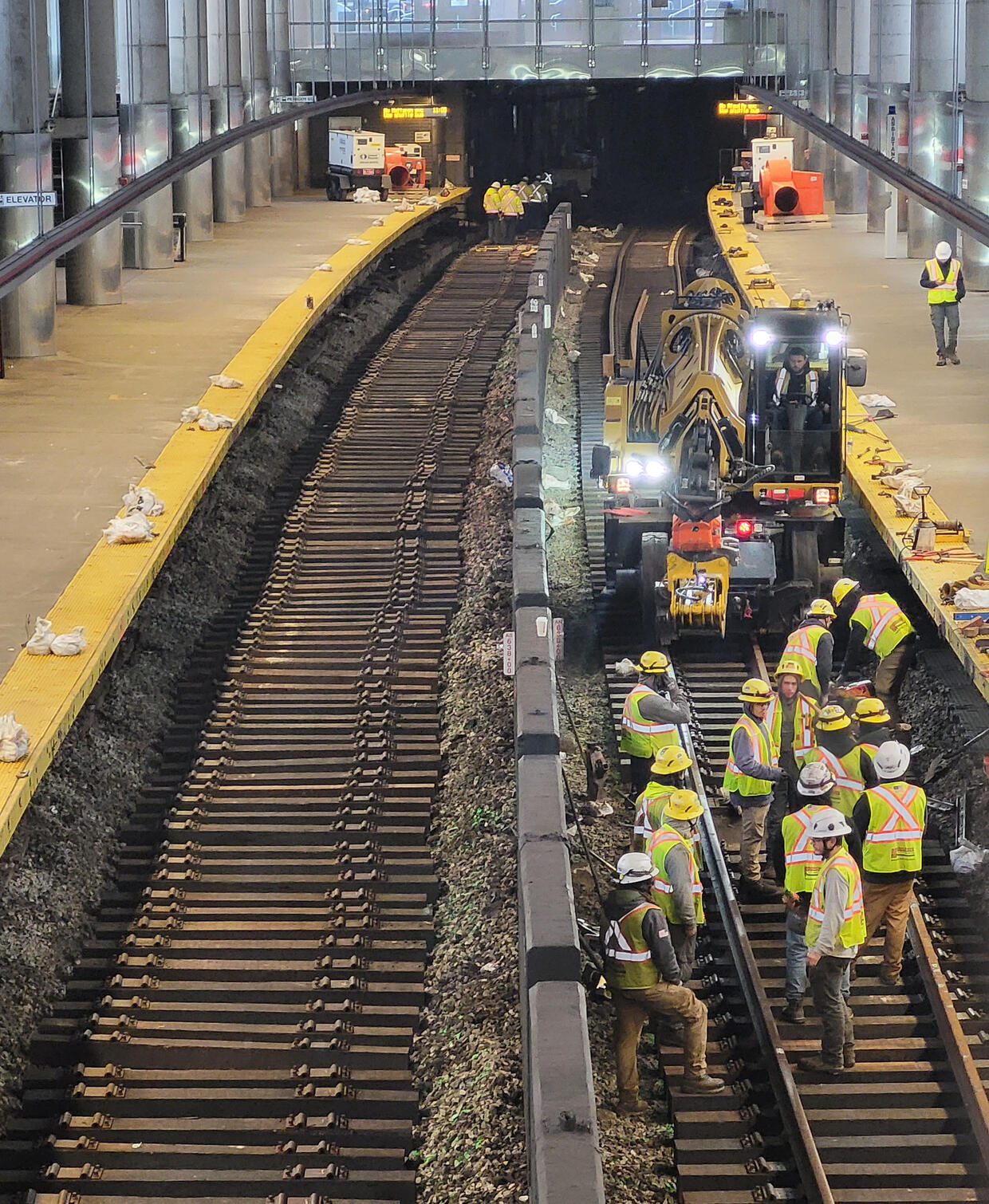 MBTA contractors in yellow and orange vests performing construction activities on railroad tracks