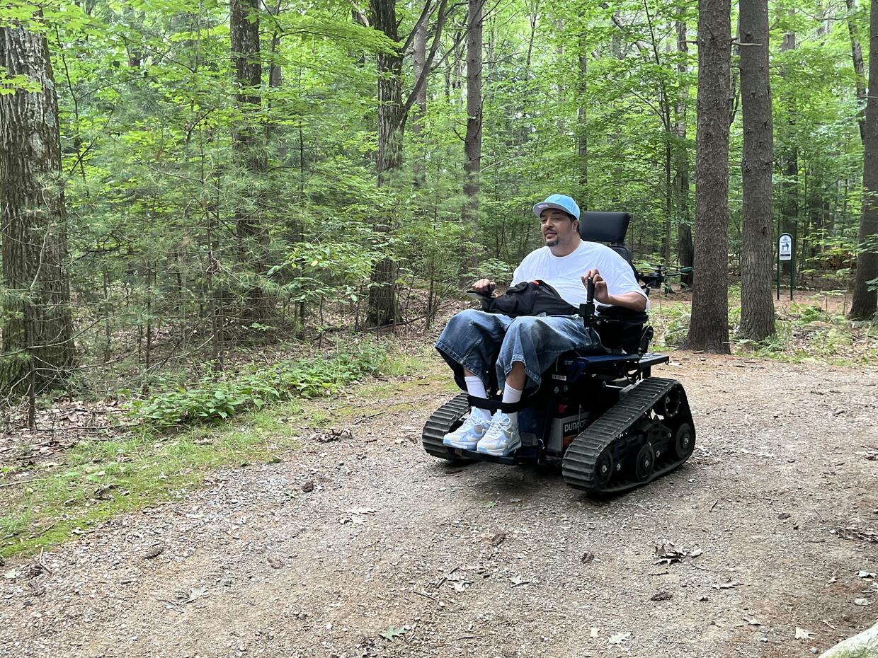 A person is riding a track chair on a trail in the woods.