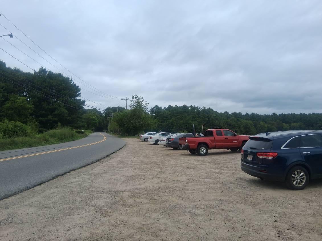 A large gravel parking area right off the road with several cars parked