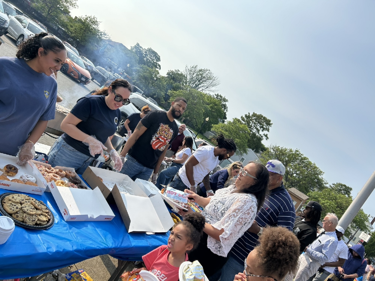 Employees serve dessert from a long table to attendees outside.