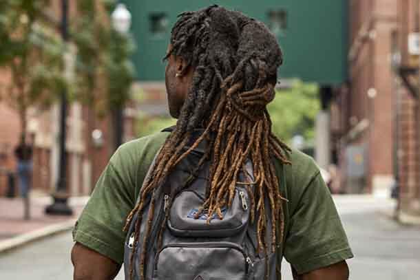A person with long dreads and a backpack walking down aa city street..