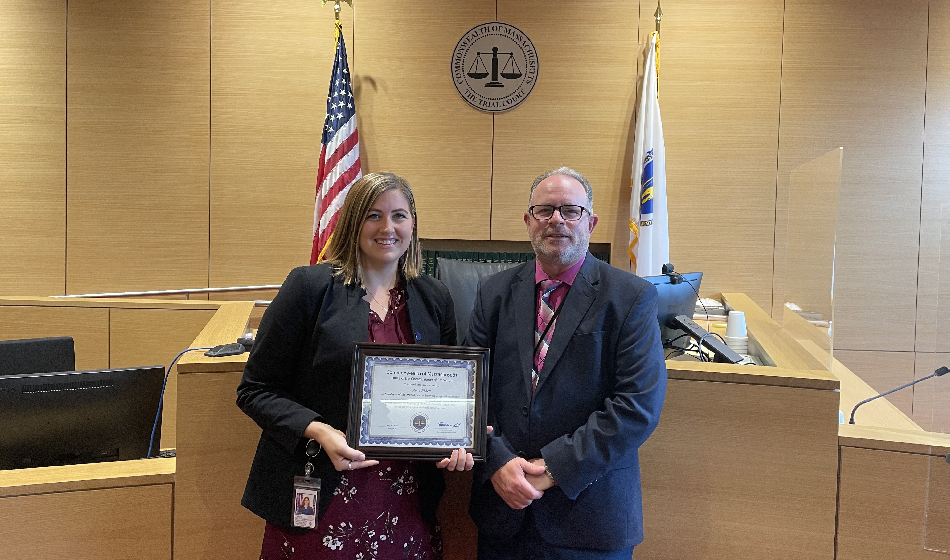 A woman holding a framed certificate poses with a man in a court room
