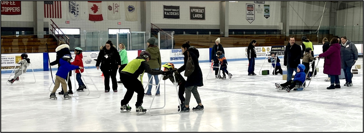 A group of people are skating and playing on the ice. Some are using skate walkers and some are seated in ice sleds. 