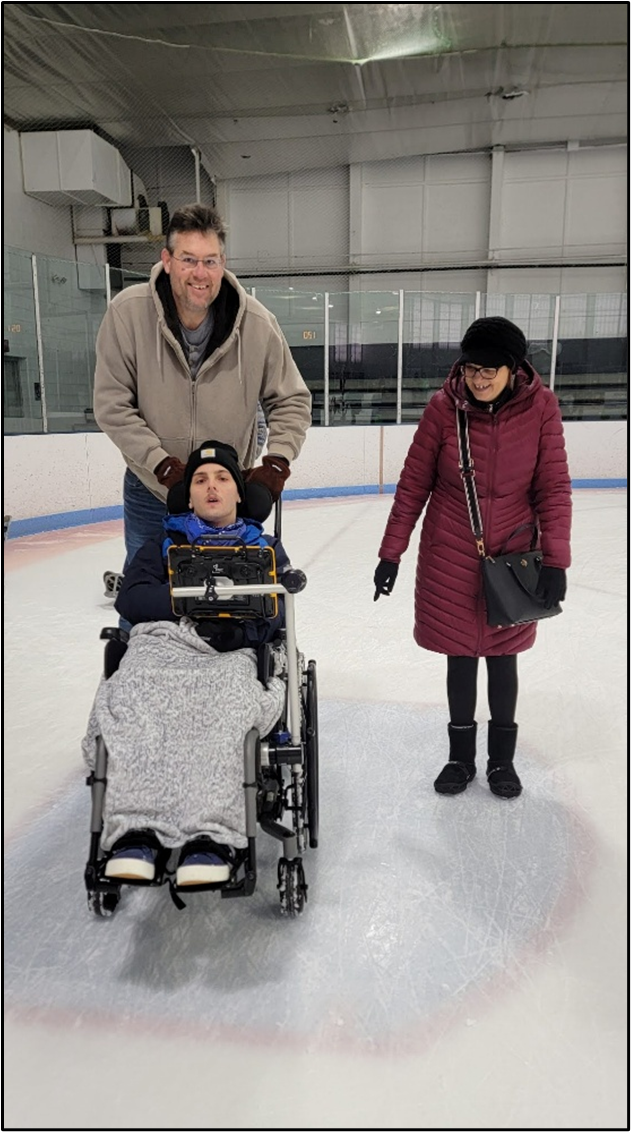 A young adult seated in his wheelchair is being pushed on the ice by his parents. 