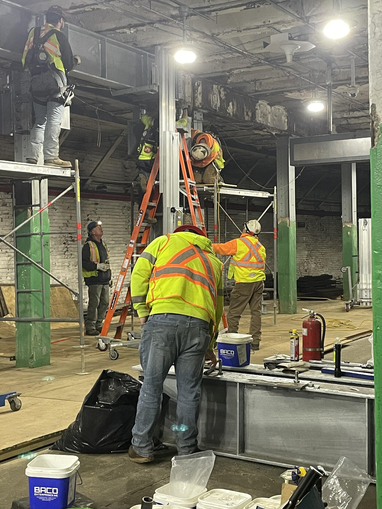 Workers in yellow and orange safety vests perform construction activities.