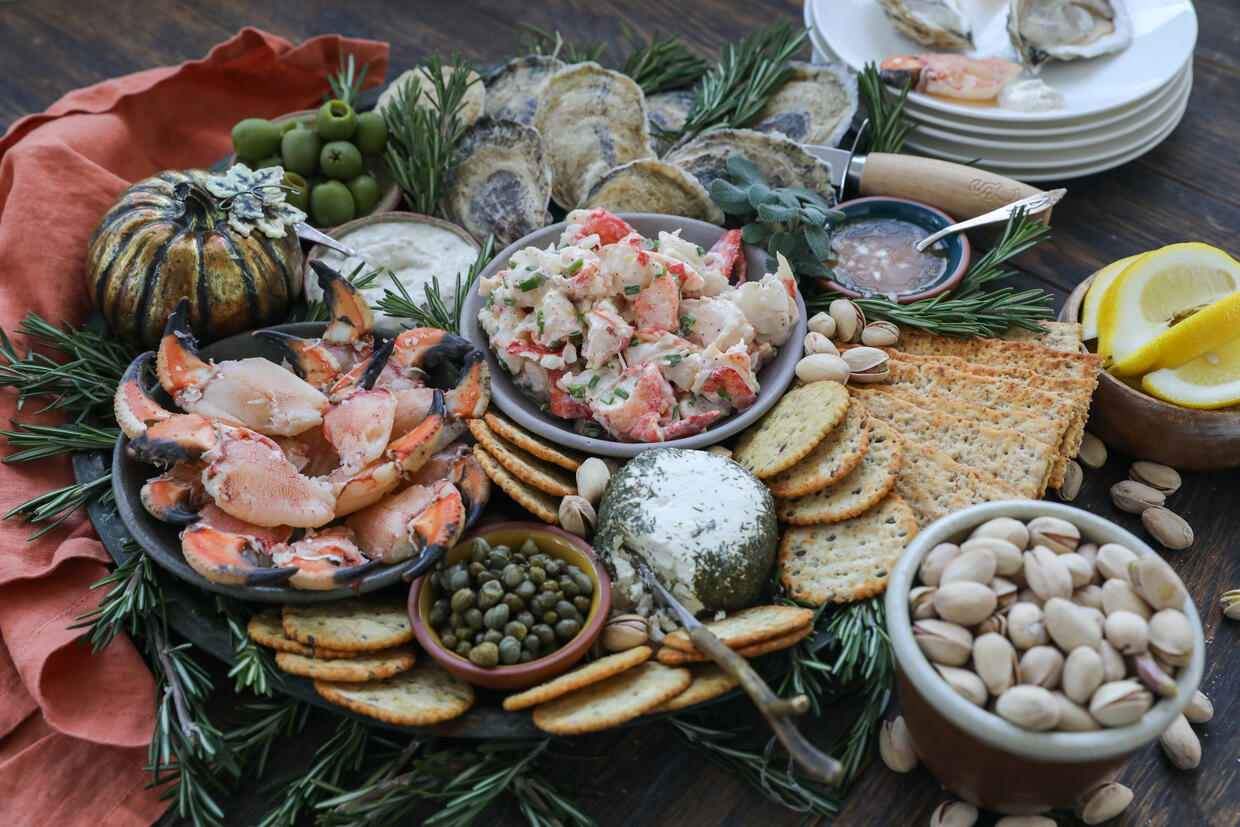 Serving platter with bowls of Jonah crab claw meat, lobster salad, and fresh oysters on the halfshell, surrounded by cheese and crackers. 
