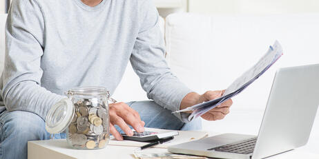 A person reviewing financial documents while using a calculator and laptop.