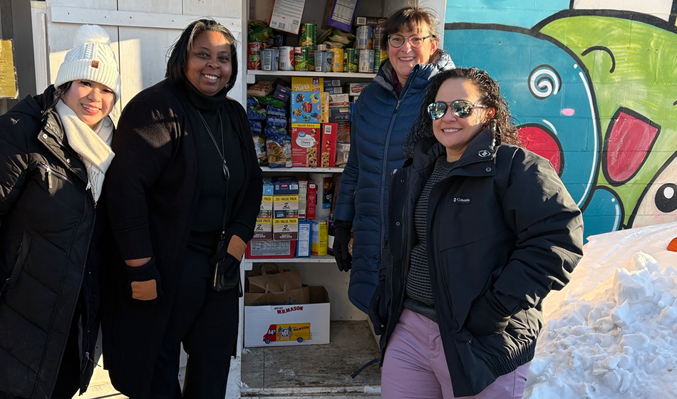 Four employees stand outside in the snow next to donations