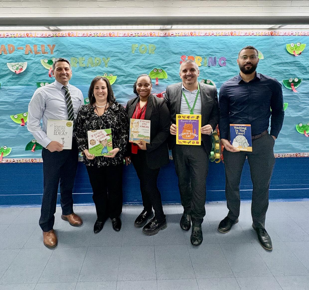 Five people standing in a school holding children's books