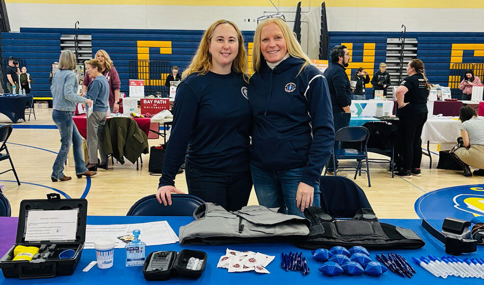 Two people in a school gym set up for a career fair with tables of giveaways.