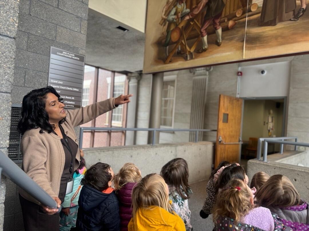 A woman points to a painting while a group of children look on.