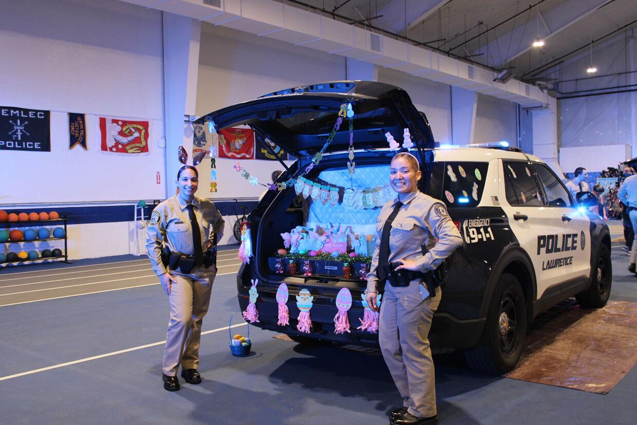 Two student officers pose in front of a police vehicle's open trunk area that has been decorated with an Easter theme.
