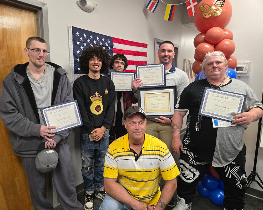 A group of people holding certificates in a hallway decorated with balloons and flags.