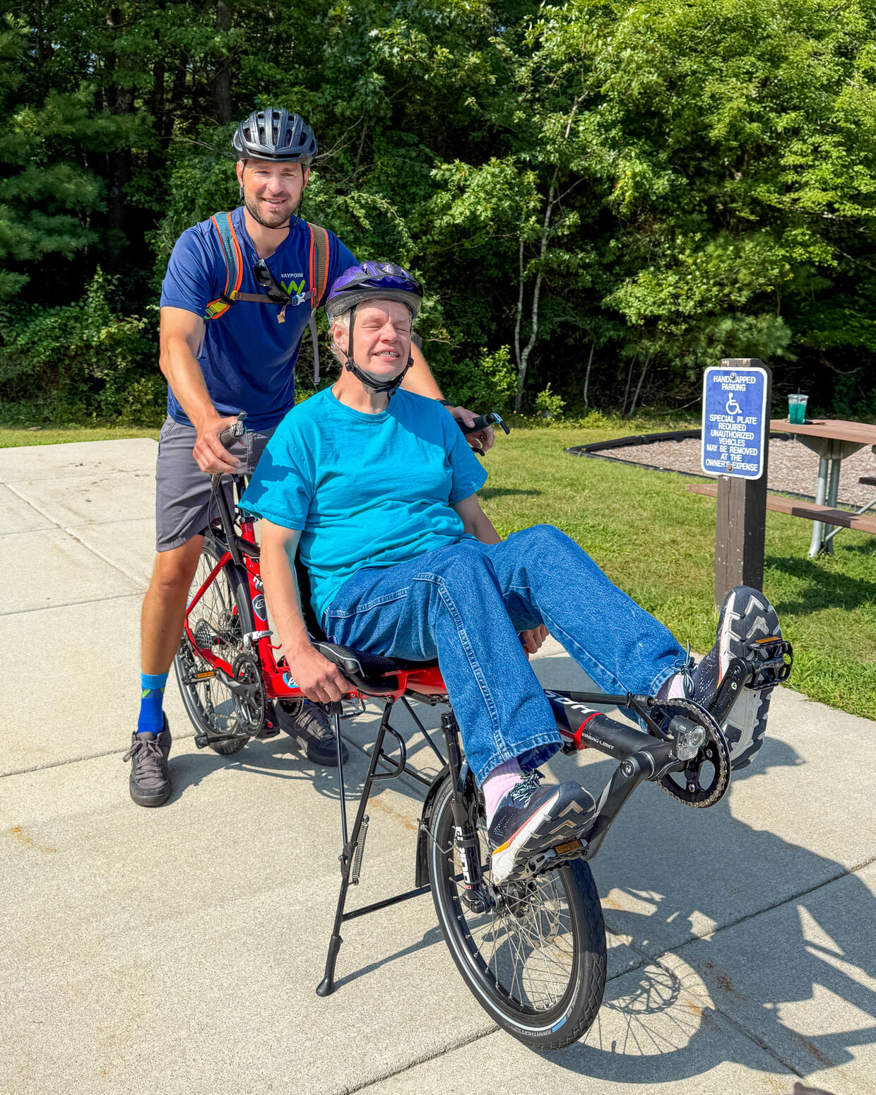 Two people riding a semi-recumbent tandem cycle smile while taking a break. 