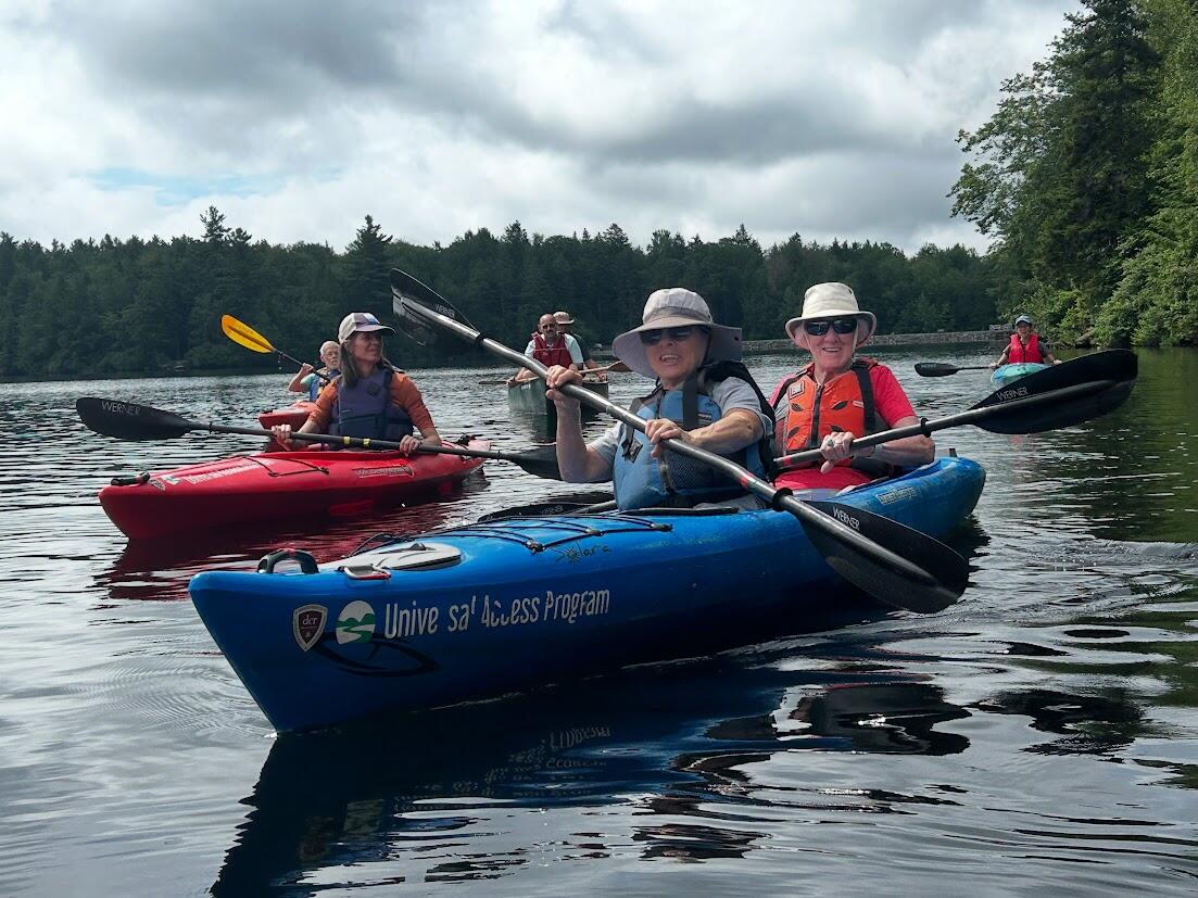 A group of people in tandem kayaks are paddling on a pond. 