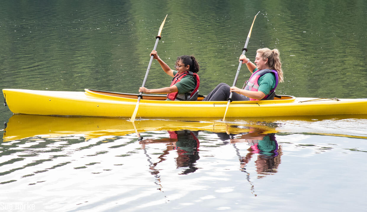 Two people in a tandem kayak are paddling on a pond. 
