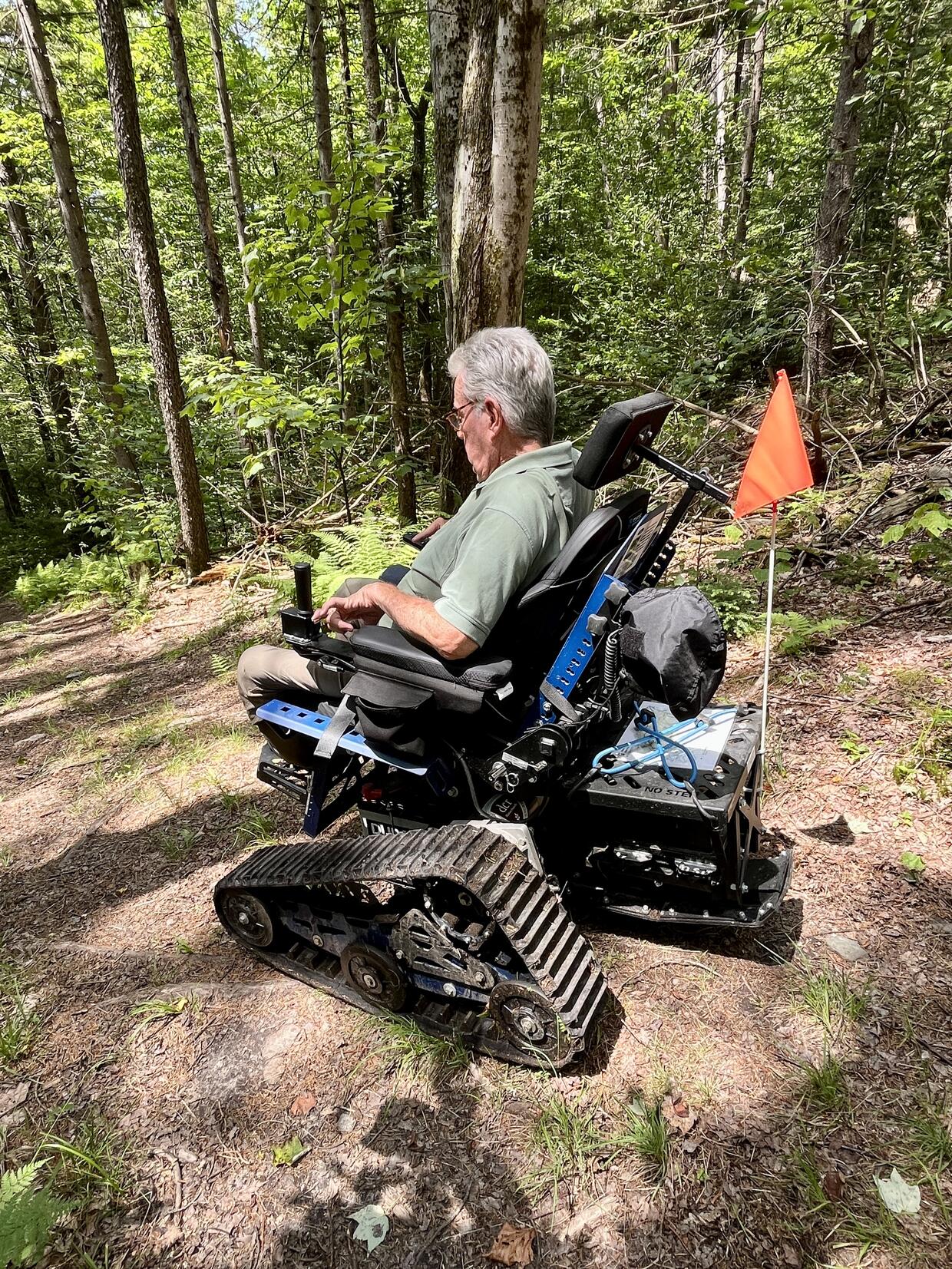UAP Director rides a Trackchair along a trail in the woods. 