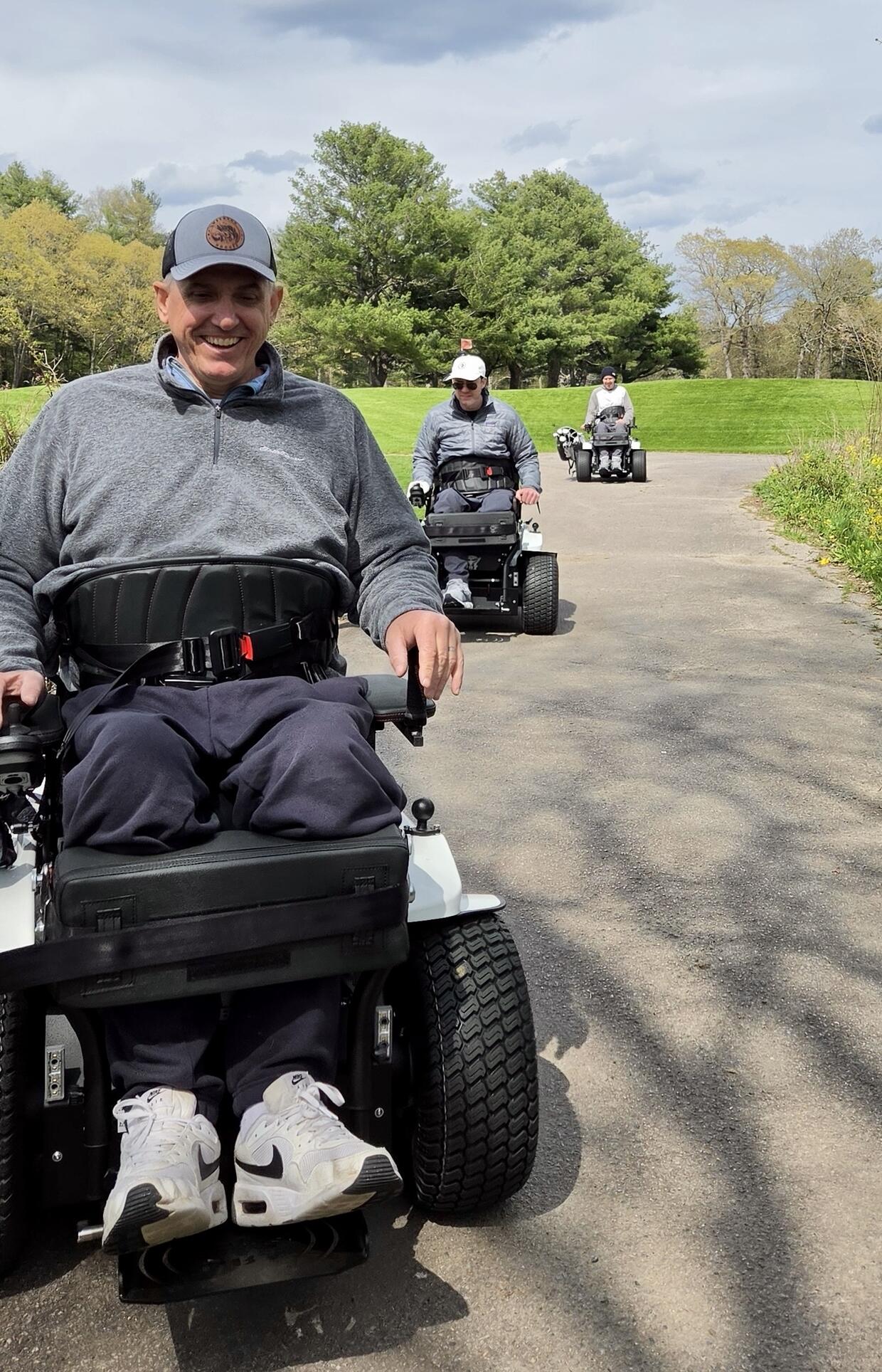 Three golfers are riding ParaMotion carts along a golf course path