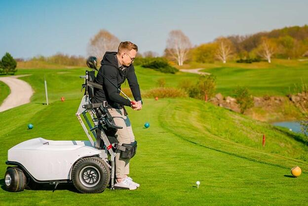 Golfer is using a ParaMotion cart to raise to a standing position to swing a golf club on a golf course. 