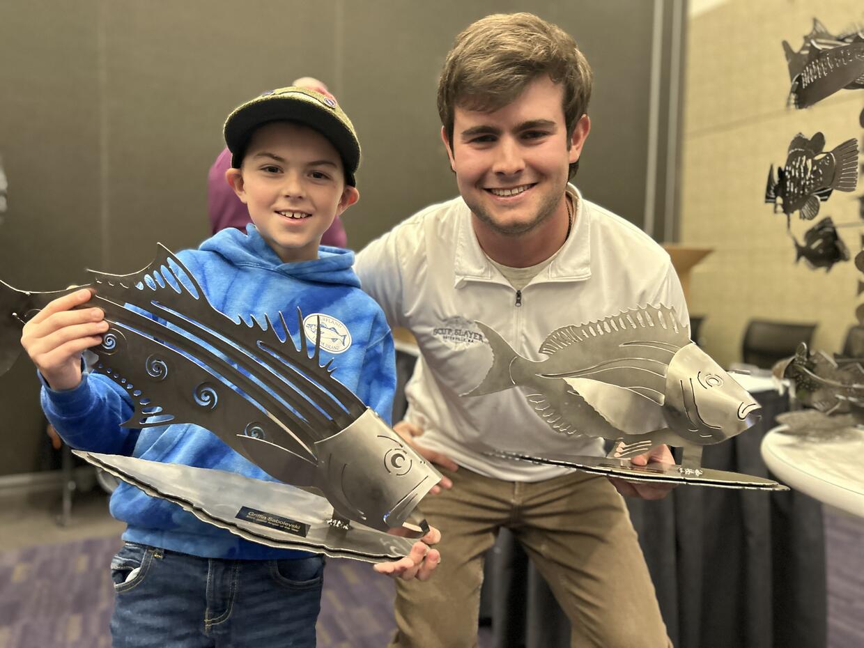 A man and a boy hold up their Angler of the Year trophies at a derby award ceremony.