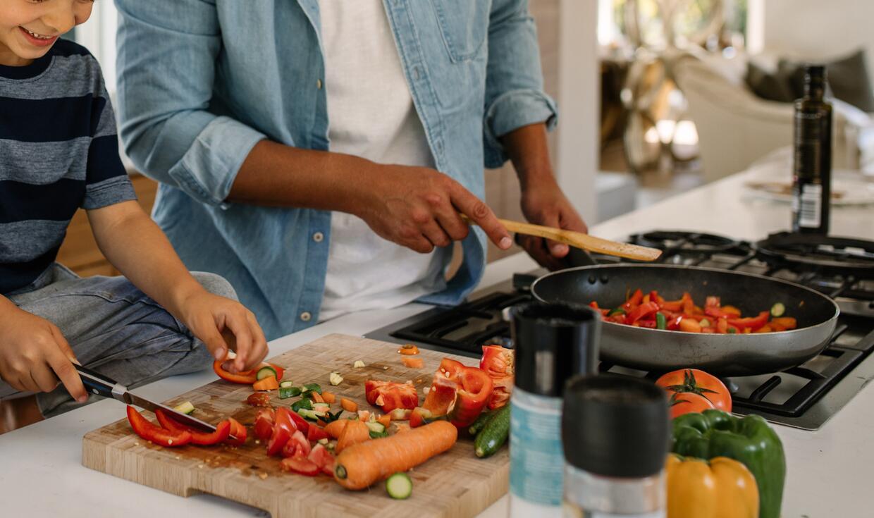 Man and child cutting vegetables and sautéing them in a pan