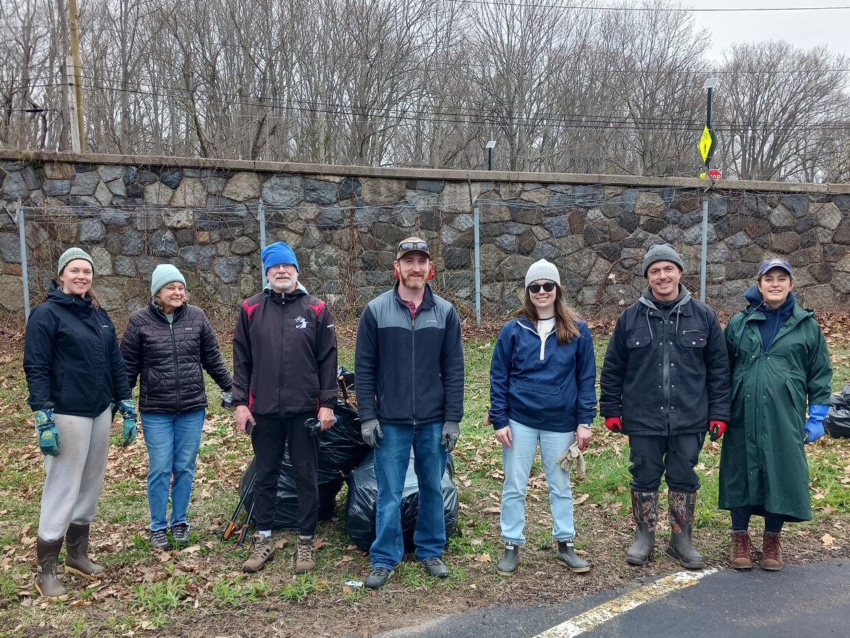 A small group of being stand outside in front of large trash bags full of plants. 