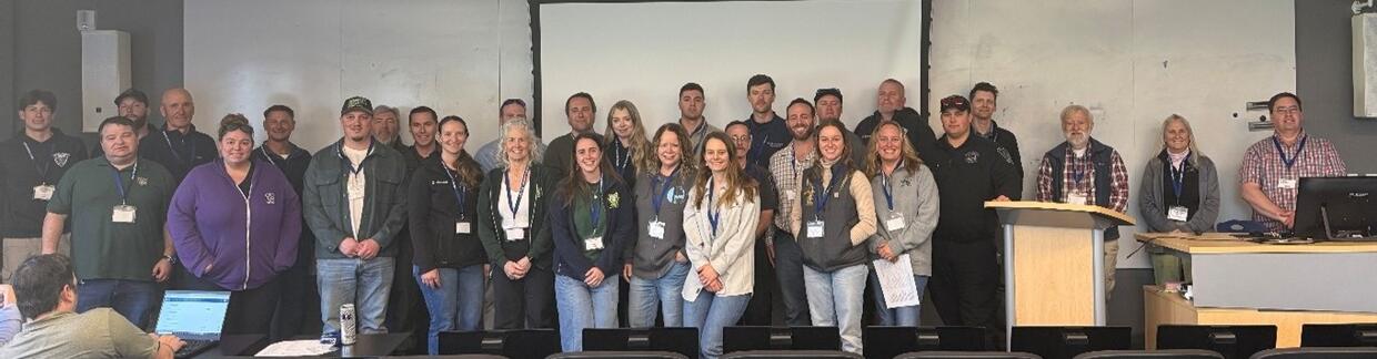 Large group of people stand together smiling in a classroom. 
