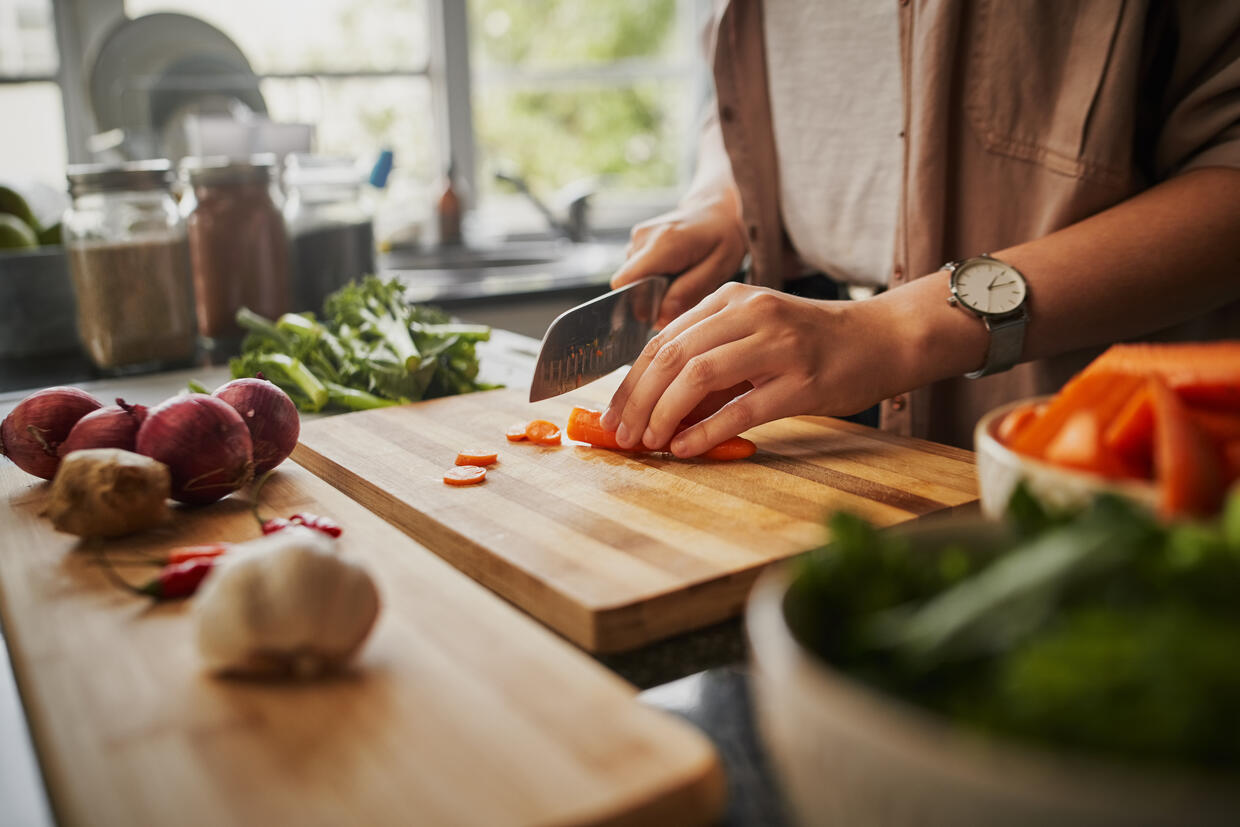 Adult chopping produce on a wooden cutting board