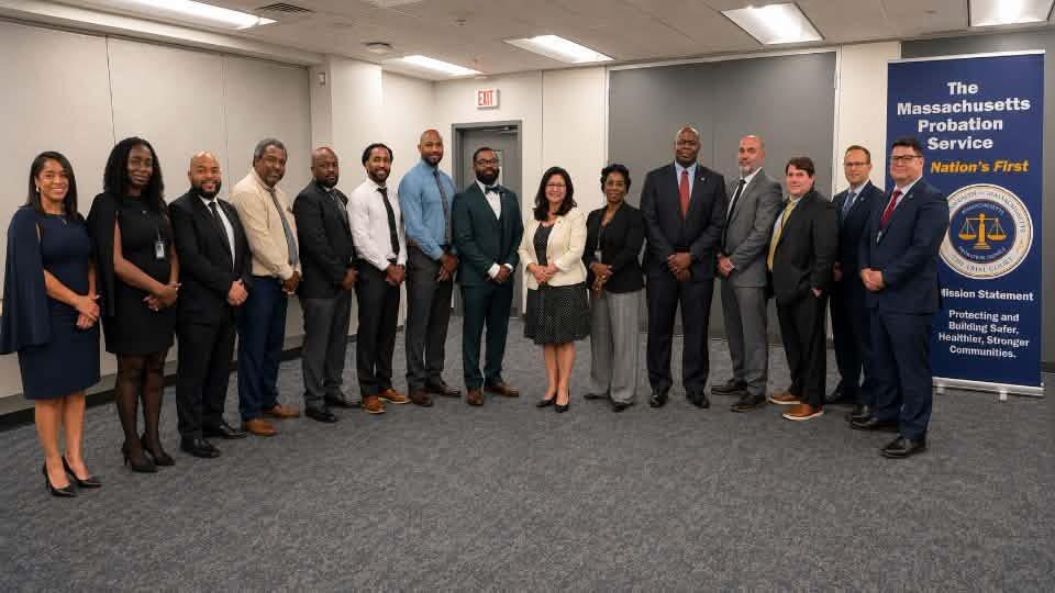 A diverse group of twelve people in professional attire stands in a line, with a banner for the Massachusetts Probation Service in the background.
