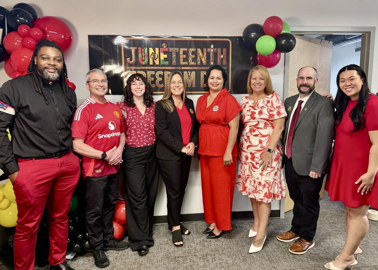 Eight people standing in front of a Juneteenth banner and balloons.