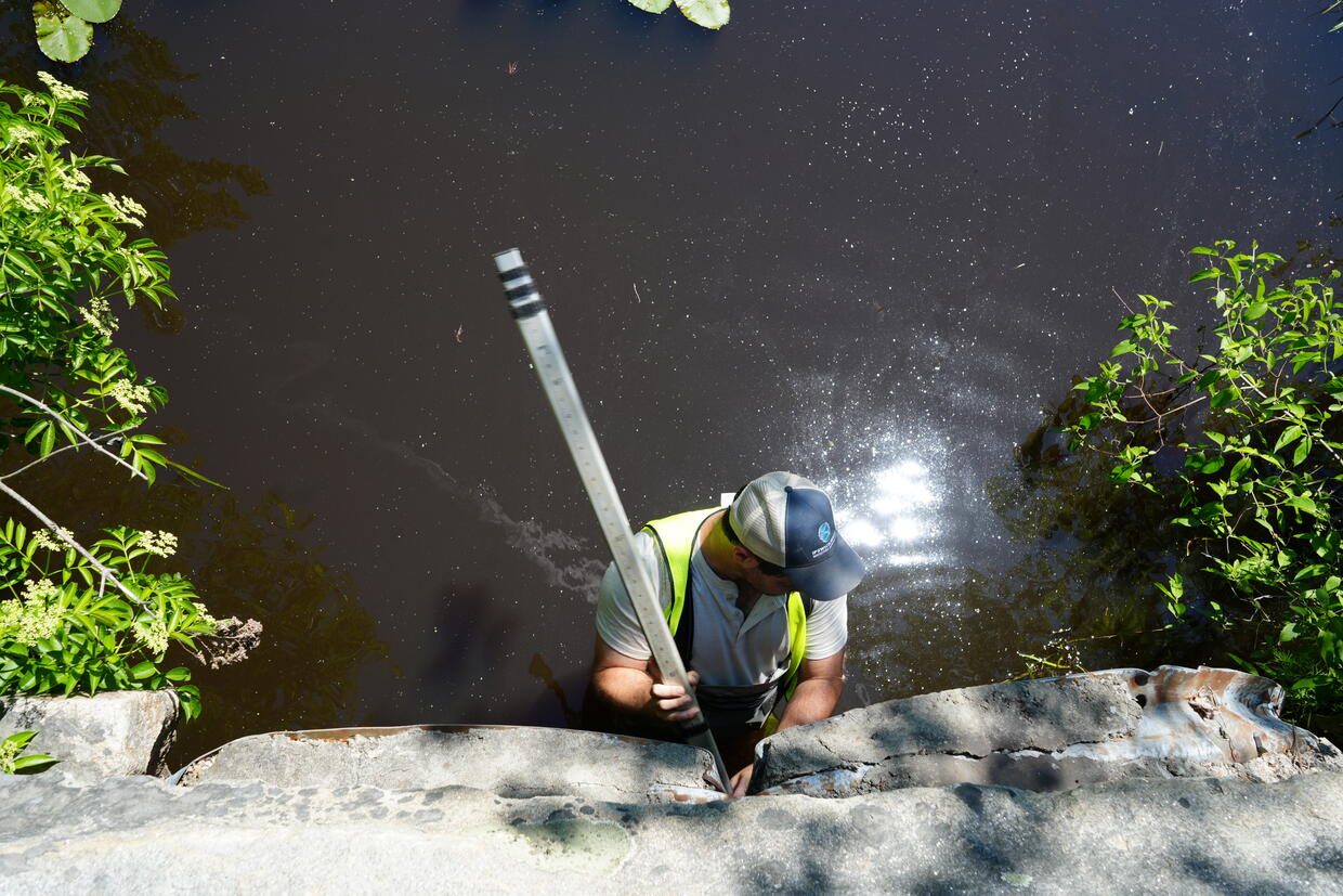 A person, viewed from above, standing in waist-high water and take a depth measurement.