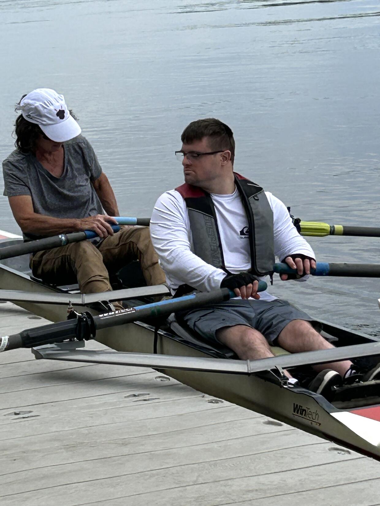 Two people in a tandem scull alongside  a river dock prepare to start paddling.  