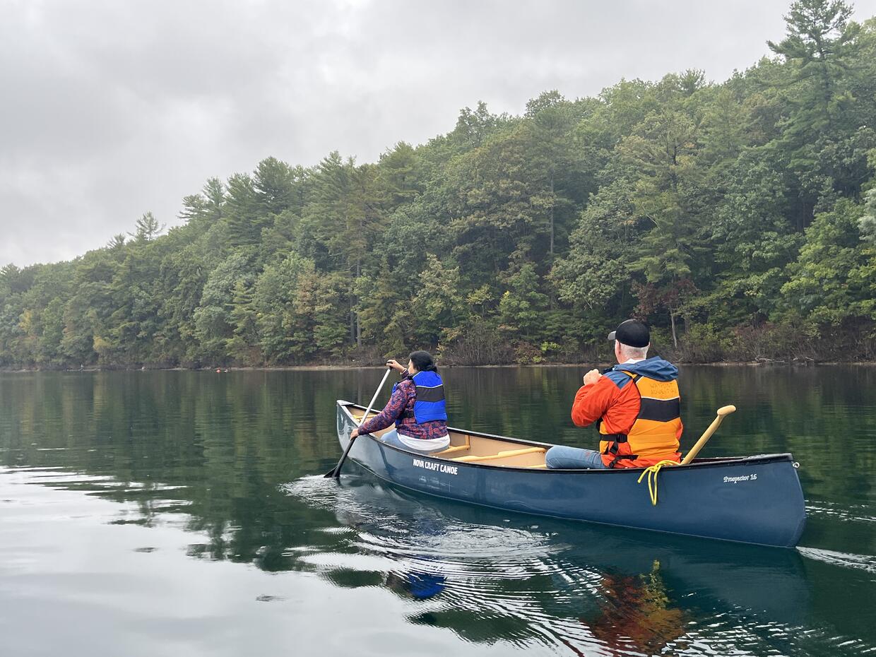 Two people are padding in a canoe on a lake in the woods. 