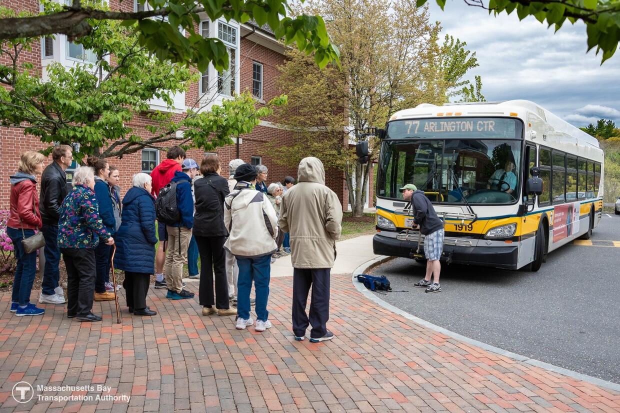 Group of older adults gathered around MBTA bus to observe demonstration of the bus’s accessibility features during the travel training event in Lexington
