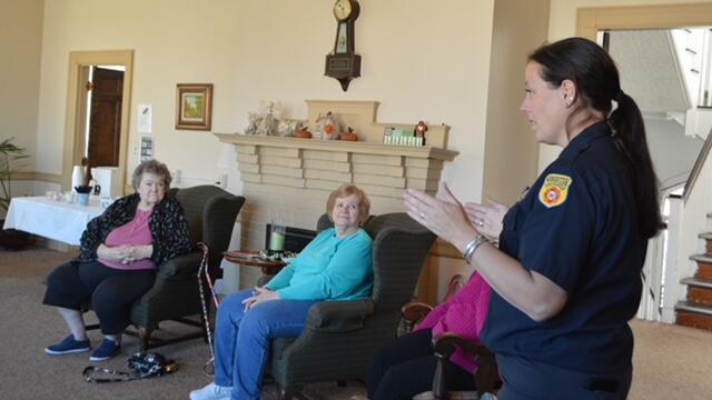 A firefighter speaks to three older residents in their living room about fire safety