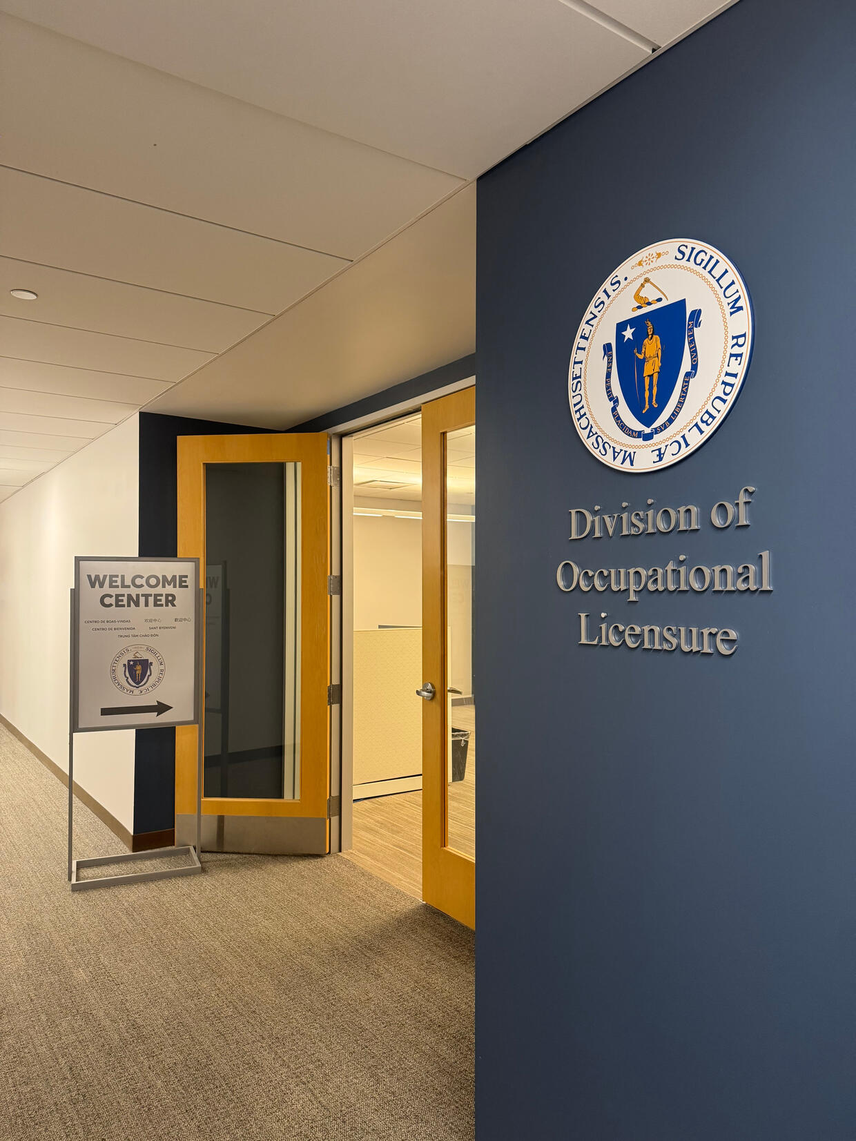 The entrance to the "Division of Occupational Licensure" with the Massachusetts state seal on the wall. A sign below reads "Welcome Center."