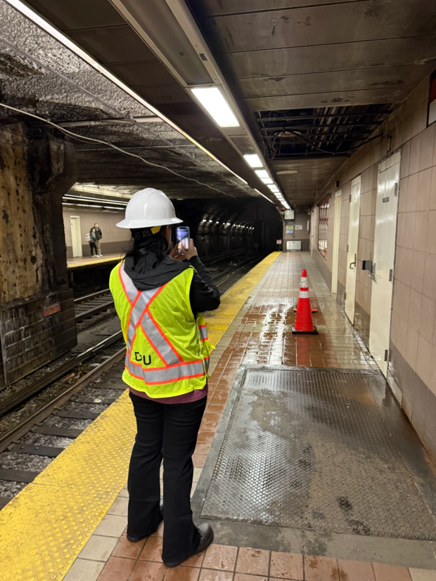DPU Compliance Officer in a yellow and orange vest takes a picture of the platform