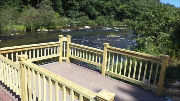 A photo of a platform that extends out over a river. The railings are at two heights,. The deck extends out under the bottom railing to provide toe clearance for a fisherperson who us using a wheelchair.