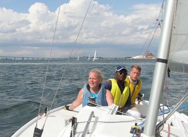 Inky in a life vest and sailboat with two other individuals 