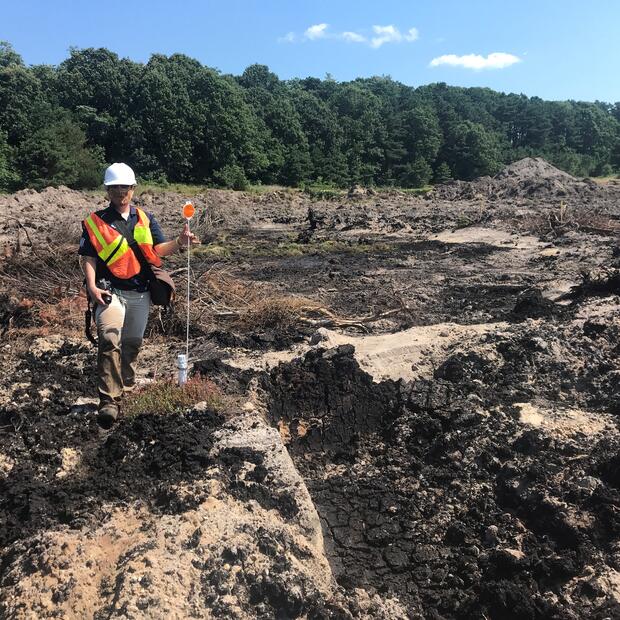 A person wearing a hard hat and high visibility vest standing in an area of disturbed earth.