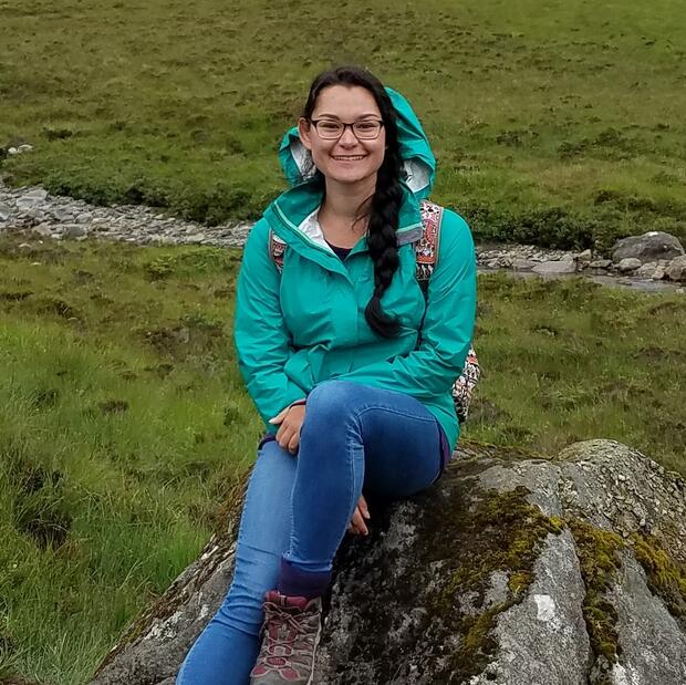 Sequoya sitting on a rock in a field and smiling at the camera.