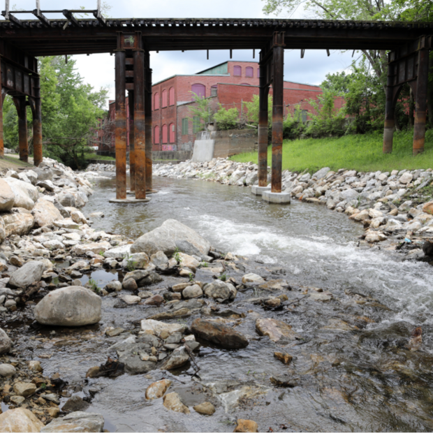 Water running underneath an old bridge and lined by large rocks.