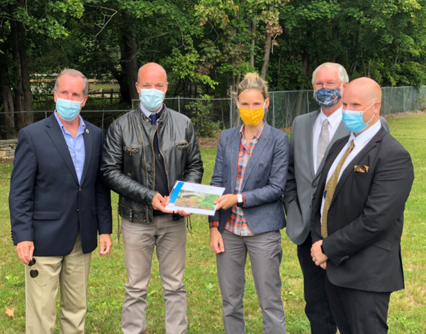 Five people posing with a paper report and wearing masks.