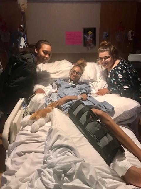 Amber Ward in hospital bed with friends on either side. Photo courtesy of Amber Ward. 