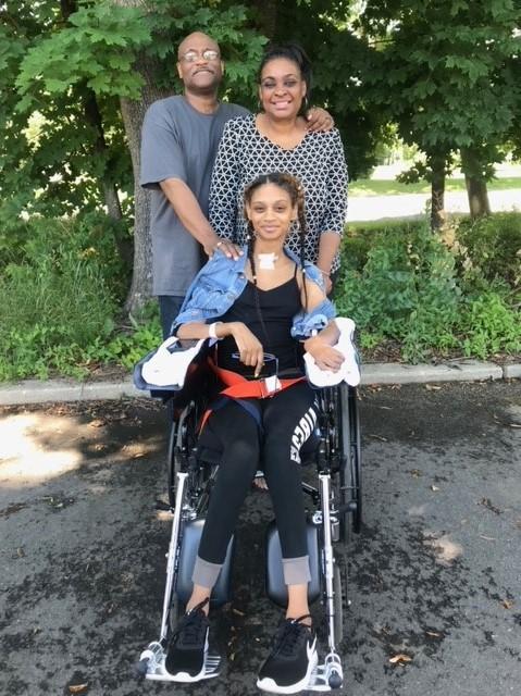 Amber Ward in a wheelchair outdoors with her parents James and Ava Ward.