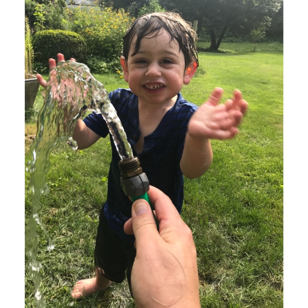 Image of a young boy with CVI outdoors playing in water from the garden hose