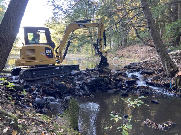 An excavator removing a small stone dam.